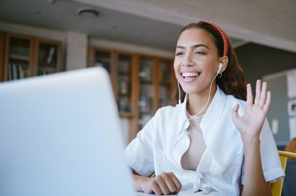 South American woman smiling and waving at a laptop screen while on a webinar