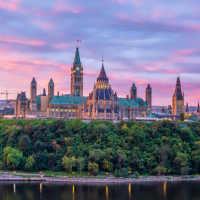 the Parliament Hill buildings in Ottawa, Canada, are silhouetted against a vibrant pink and purple sunset sky, with a river and lush green trees in the foreground