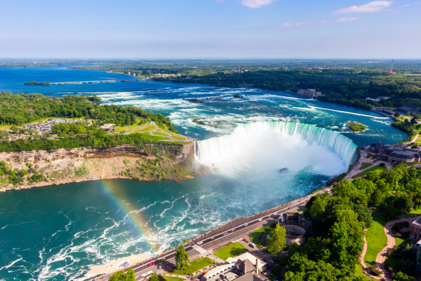 an aerial view of Niagara Falls with a rainbow in the mist and lush green trees surrounding the area