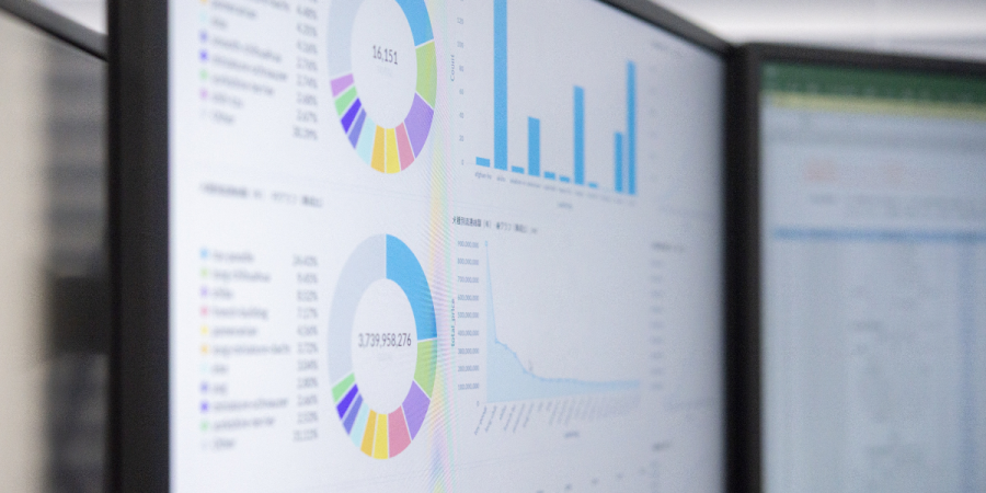 two computer monitors displaying various charts and graphs, including pie charts, bar graphs, and line graphs, indicating data analysis and financial reporting.