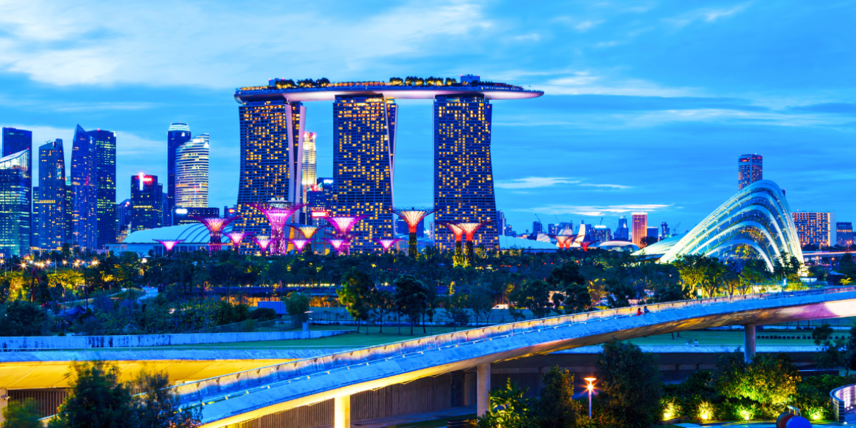 The Singapore skyline at twilight, featuring the Marina Bay Sands hotel, Gardens by the Bay, and other illuminated skyscrapers.