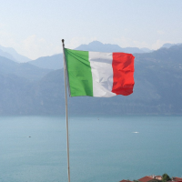 Green, white, and red tricolour flag waving on a tall pole against a clear blue sky with scattered clouds.
