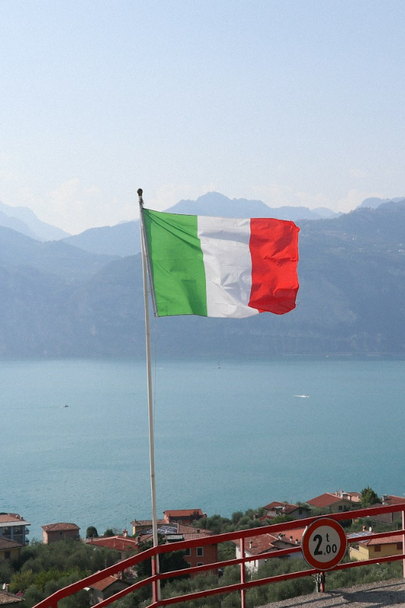 Green, white, and red tricolour flag waving on a tall pole against a clear blue sky with scattered clouds.