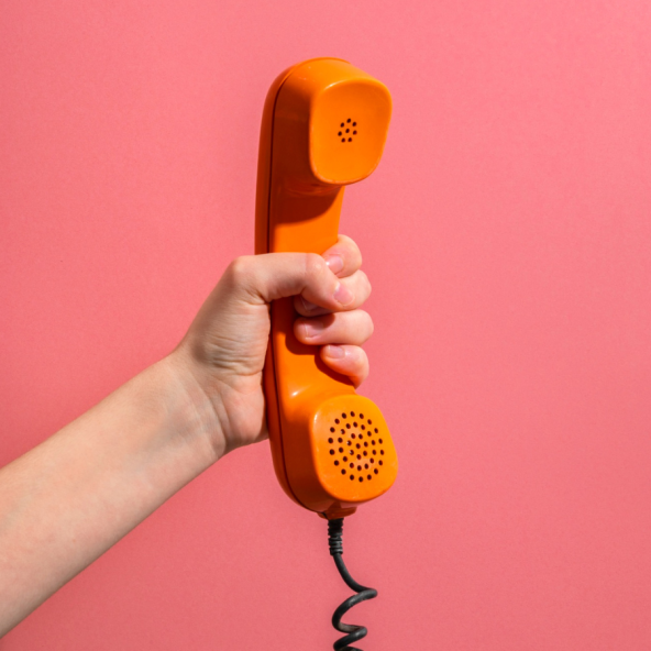 a close-up of a hand holding an onrange phone against a coral pink background