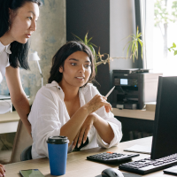 two Asian women collaborating on a project at a desk with a computer