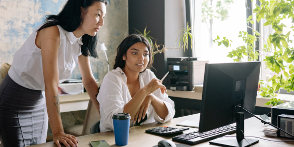two Asian women collaborating on a project at a desk with a computer