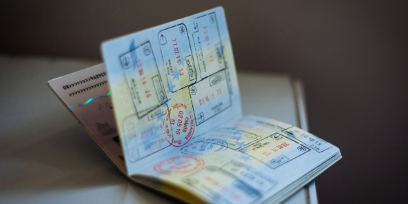 A passport opened on a table with several overlapping visas and stamped travel documents, including a prominently visible blue form and colourful entry/exit stamps.