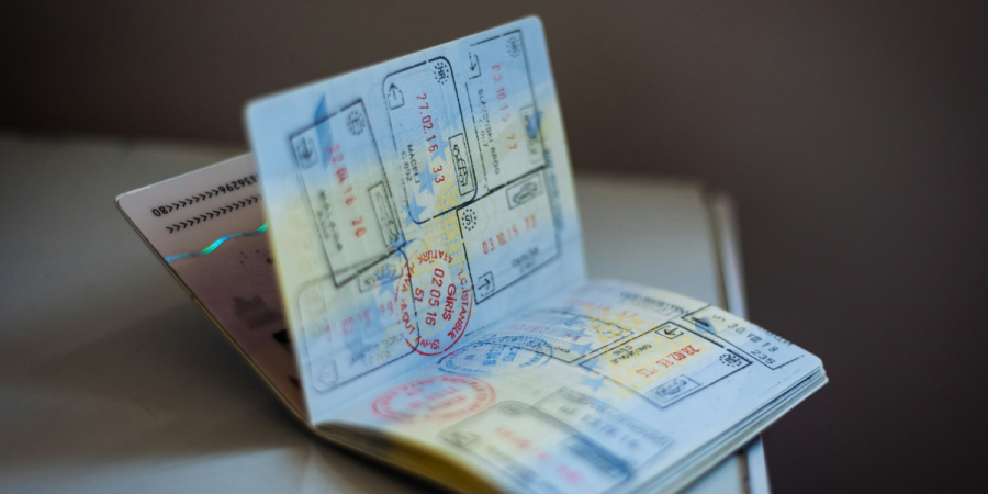 A passport opened on a table with several overlapping visas and stamped travel documents, including a prominently visible blue form and colourful entry/exit stamps.
