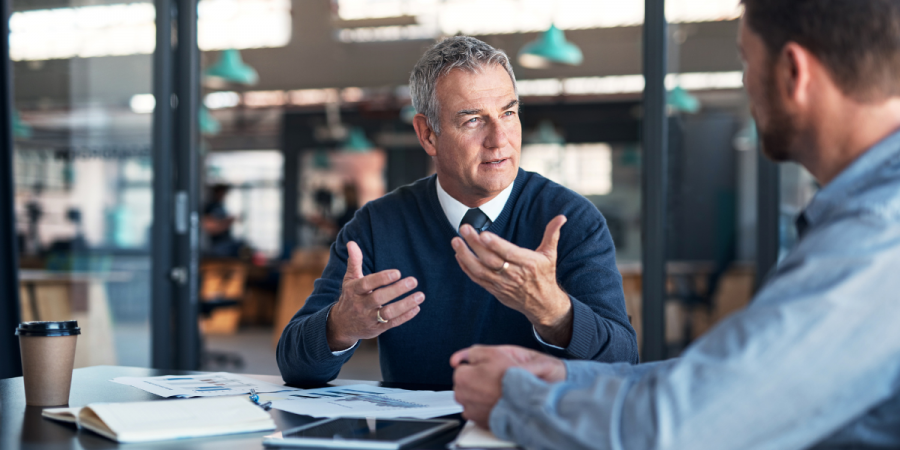 Senior male professional in navy jumper talking to his colleague