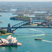 Aerial view of Sydney Harbour, featuring the Sydney Opera House and Sydney Harbour Bridge with boats on the water and a cityscape in the background