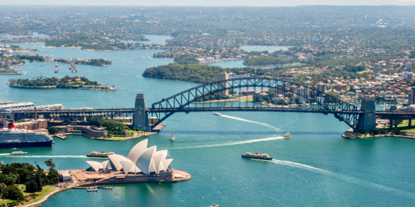Aerial view of Sydney Harbour, featuring the Sydney Opera House and Sydney Harbour Bridge with boats on the water and a cityscape in the background