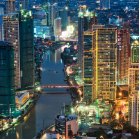 A night time aerial view of a city skyline with a river flowing through it, illuminated by the lights of numerous skyscrapers and streetlights