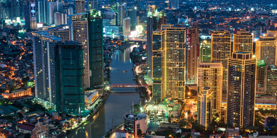 A night time aerial view of a city skyline with a river flowing through it, illuminated by the lights of numerous skyscrapers and streetlights