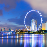 a cityscape at dusk with a large Ferris wheel illuminated by white lights, reflecting on the water in the foreground