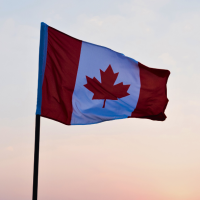the Canadian flag, red and white with a red maple leaf, waves on a flagpole against a clear blue sky