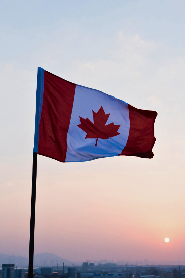 the Canadian flag, red and white with a red maple leaf, waves on a flagpole against a clear blue sky