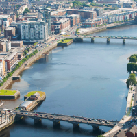 an aerial daytime view of a wide river flowing through a city with bridges, buildings, and greenery along its banks.