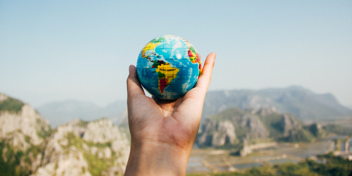 man holding a globe figure against scenic background