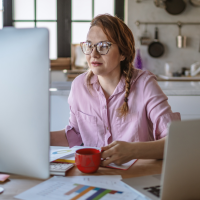 woman wearing a pink shirt, remote working from her kitchen desk
