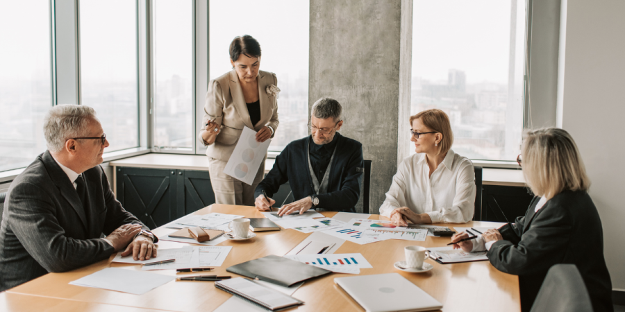 a group of senior leadership professionals in a conference room with documents spread across a table