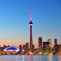 the Toronto skyline at dusk, featuring the CN Tower illuminated in pink and purple lights, with a body of water in the foreground and a clear blue sky above