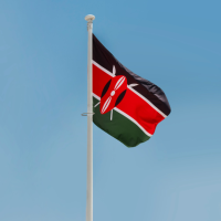 The Kenyan flag waves against a clear blue sky, attached to a white flagpole.