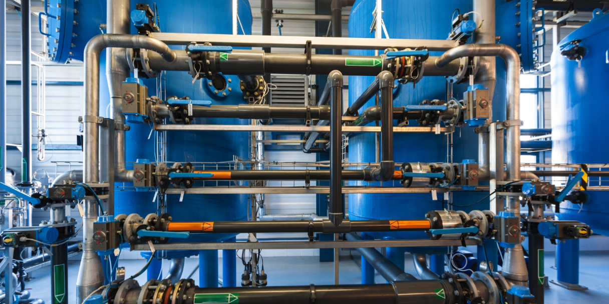 Industrial blue and stainless-steel piping system with multiple valves, gauges, and control components mounted on a large frame inside a clean facility.