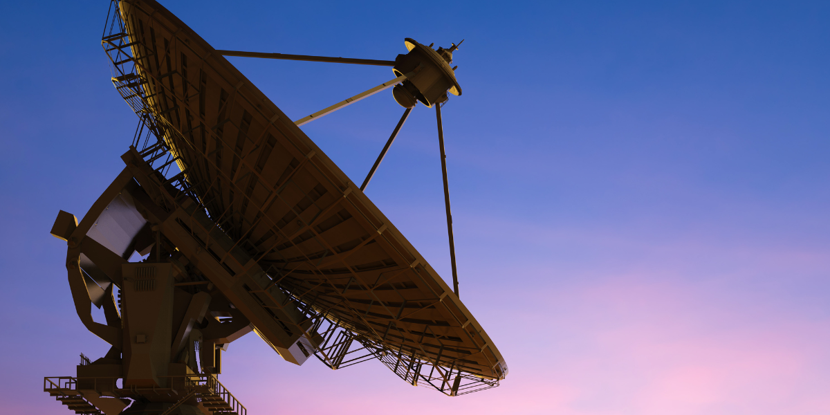 Large radio telescope dish on a metal support structure, tilted toward the sky at dusk with a deep blue and pink gradient background.