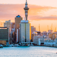 the Auckland skyline at sunset, featuring the Sky Tower and a sailboat on the water.