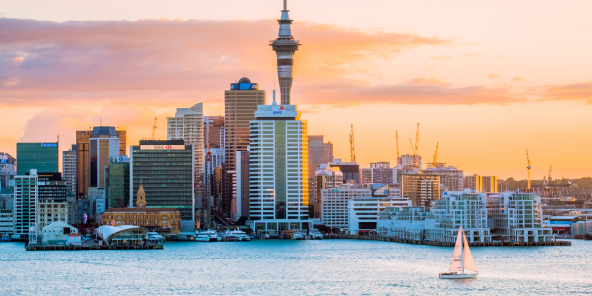 the Auckland skyline at sunset, featuring the Sky Tower and a sailboat on the water.