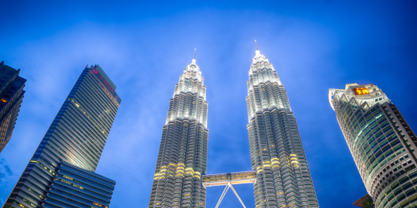 The Petronas Twin Towers in Kuala Lumpur illuminated at night against a deep blue sky.
