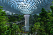 an indoor waterfall cascades from a large glass dome, surrounded by lush greenery and elevated walkways
