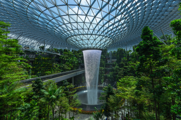 an indoor waterfall cascades from a large glass dome, surrounded by lush greenery and elevated walkways