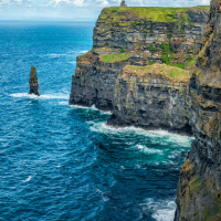 The Cliffs of Moher in Ireland are dramatic sea cliffs overlooking the Atlantic Ocean under a bright blue sky with scattered clouds.