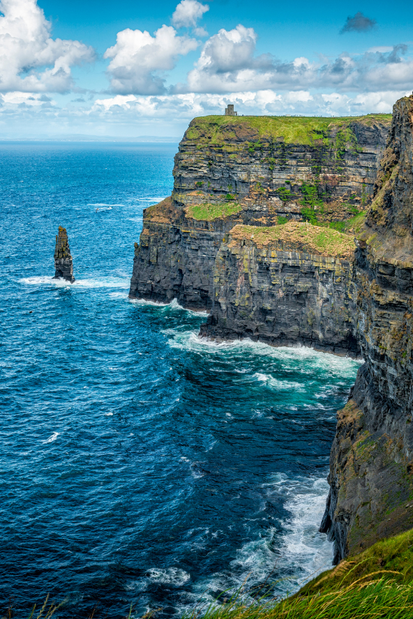 The Cliffs of Moher in Ireland are dramatic sea cliffs overlooking the Atlantic Ocean under a bright blue sky with scattered clouds.