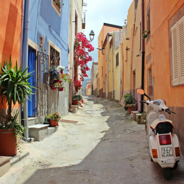 Sunny narrow italian street with colourful buildings and a moped parked outside.