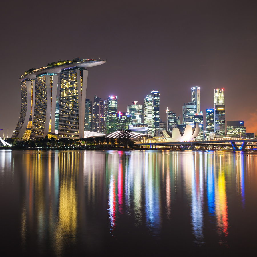 a nighttime view of the Singapore skyline, featuring the Marina Bay Sands hotel and other illuminated skyscrapers reflected in the water