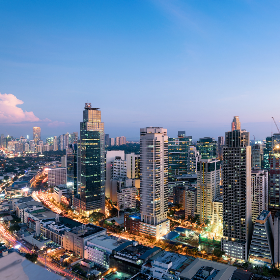 A cityscape at dusk with numerous illuminated skyscrapers under a twilight sky.