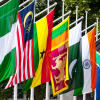 A row of colourful national and regional flags hanging from poles outdoors, including green-and-white, a red-and-white striped flag, a blue flag with a yellow emblem, and the Union Jack.