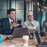 a group of professionals in business attire are gathered around a conference table, engaged in a lively discussion, with laptops and documents spread out before them