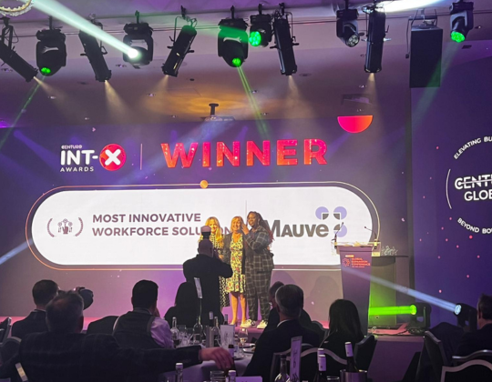 Three individuals stand on stage accepting an award for "Most Innovative Workforce Solution" presented by INT-X Awards. The award is displayed on a large screen behind them, with "WINNER" prominently featured
