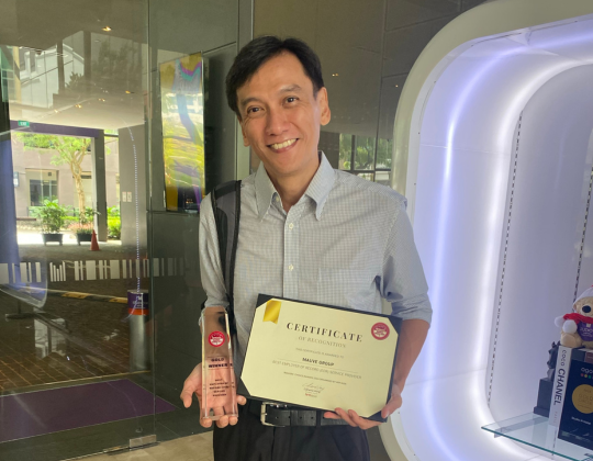 Andrew Soon proudly holds a certificate and a trophy, smiling at the camera.