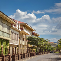 A street lined with traditional colonial-style buildings and palm trees under a cloudy blue sky.
