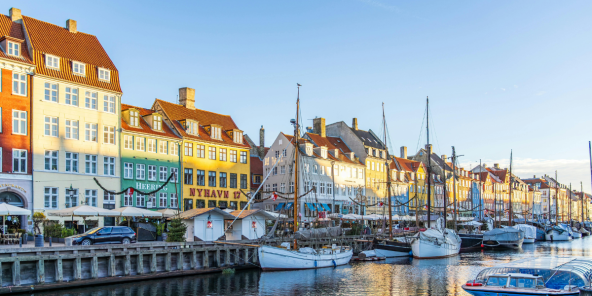 Colorful buildings line a canal in Copenhagen, Denmark, with boats docked along the waterway and reflections in the water.