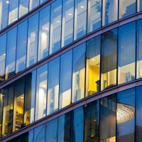 A modern office building with rows of glass windows, some illuminated from within, reflecting the blue evening sky.