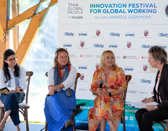 Four people are seated on chairs in front of a banner that reads "Innovation Festival for Global Working".