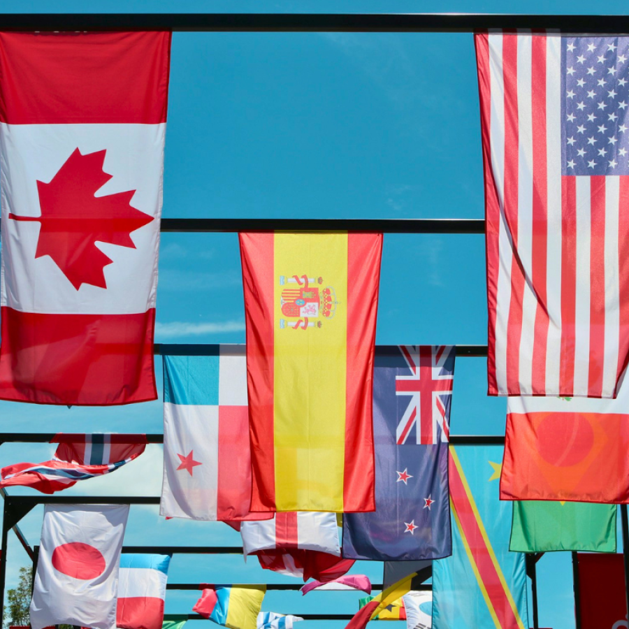 A display of international flags including Canada, Spain, the United States, Panama, New Zealand, the UK, Japan, and others against a bright blue sky.
