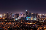 A sprawling cityscape at night, with illuminated skyscrapers in the background and densely packed residential areas in the foreground.