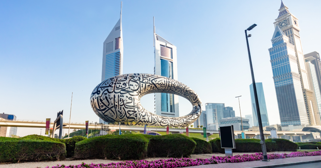 The Museum of the Future in Dubai, a torus-shaped building covered in Arabic calligraphy, stands against a clear blue sky with modern skyscrapers in the background.