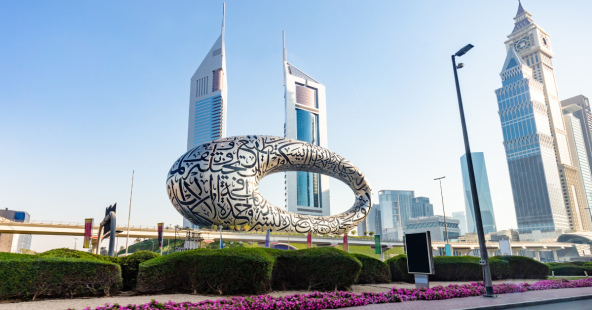 The Museum of the Future in Dubai, a torus-shaped building covered in Arabic calligraphy, stands against a clear blue sky with modern skyscrapers in the background.